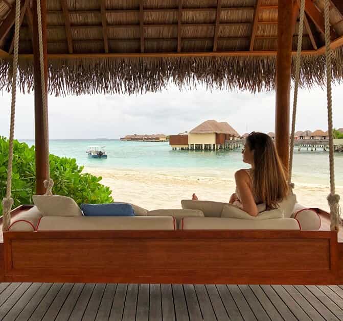 a hanging couch connected to the ceiling of a cabana located beachside